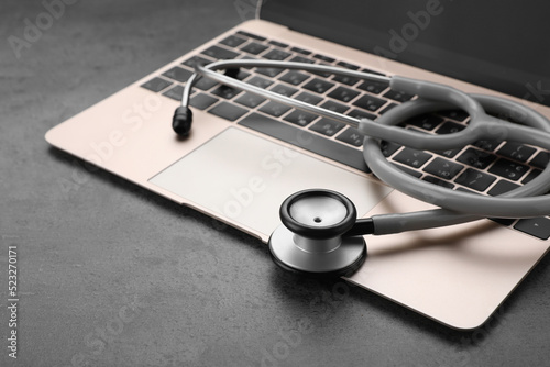 Laptop with stethoscope on grey table, closeup. Space for text