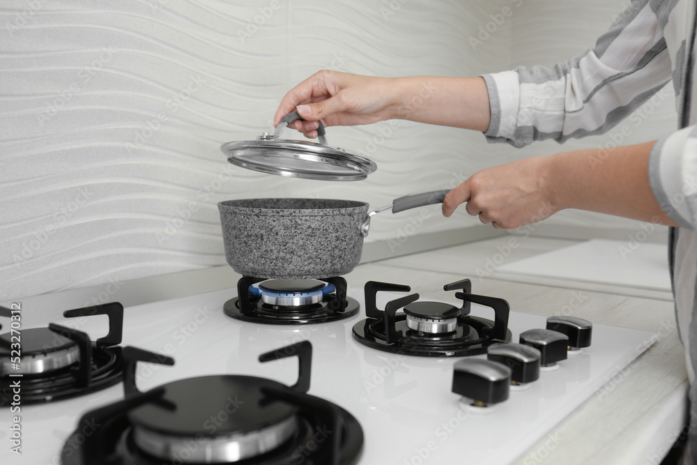Woman putting pot on gas stove in kitchen, closeup Woman putting pot on gas stove in kitchen, closeup