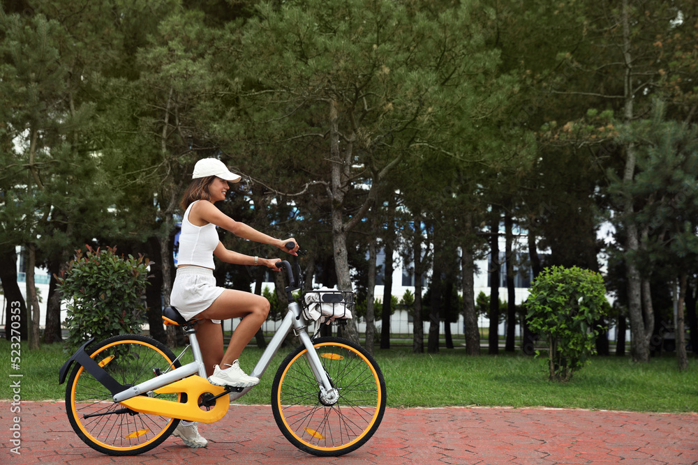 Fototapeta premium Beautiful young woman riding bicycle on lane outdoors. Space for text