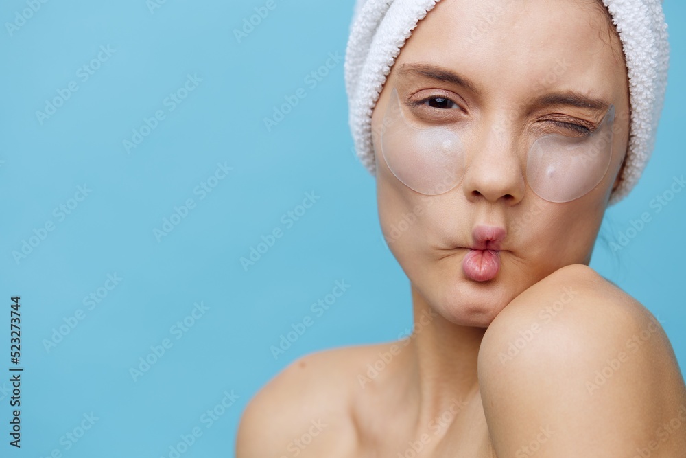 a funny woman makes a funny face pulling in her cheeks while standing on a blue background with a towel on her head and eye patches a funny woman makes a funny face pulling in her cheeks while standing on a blue background with a towel on her head and eye patches