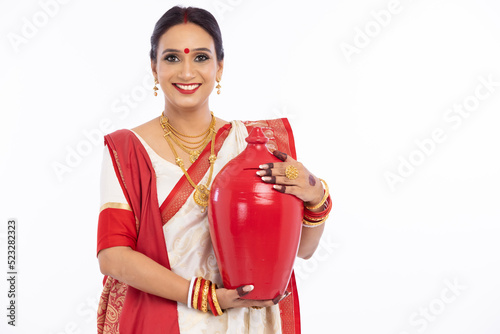 Portrait of beautiful bengali woman holding earthen piggy bank in traditional red and white sari 