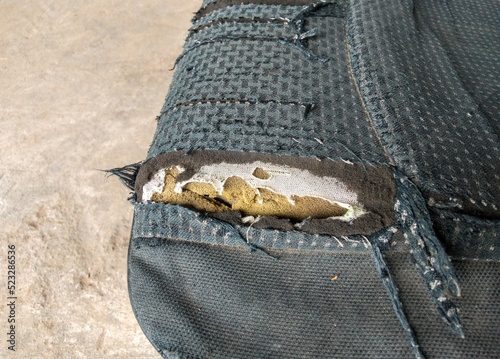 Black fabric upholstery torn, see yellow foam inside. Concept, deterioration, broken, torn, old.