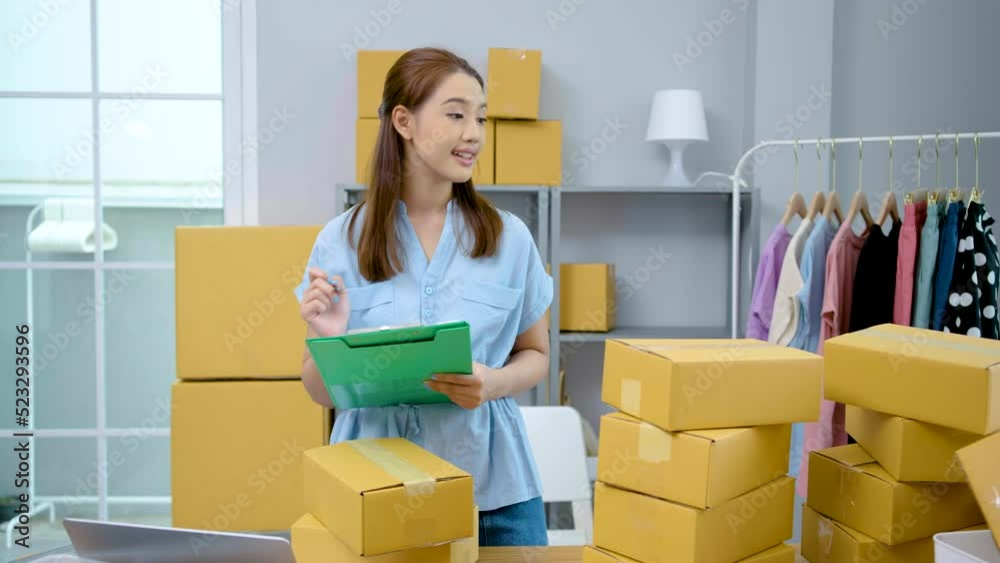 Asian business owner woman Write down the details of the product in a file while checking information about parcel and preparing sending it to the client and look at camera work happy with box at home Asian business owner woman Write down the details of the product in a file while checking information about parcel and preparing sending it to the client and look at camera work happy with box at home