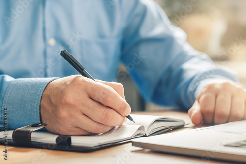 Man writes notes in his diary and planning new business goals at the table in the office, hand with a pen, close-up view