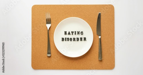 The text Eating Disorder appears on the plate. Plate, fork and knife on a cork napkin. 4K stop motion animation photo