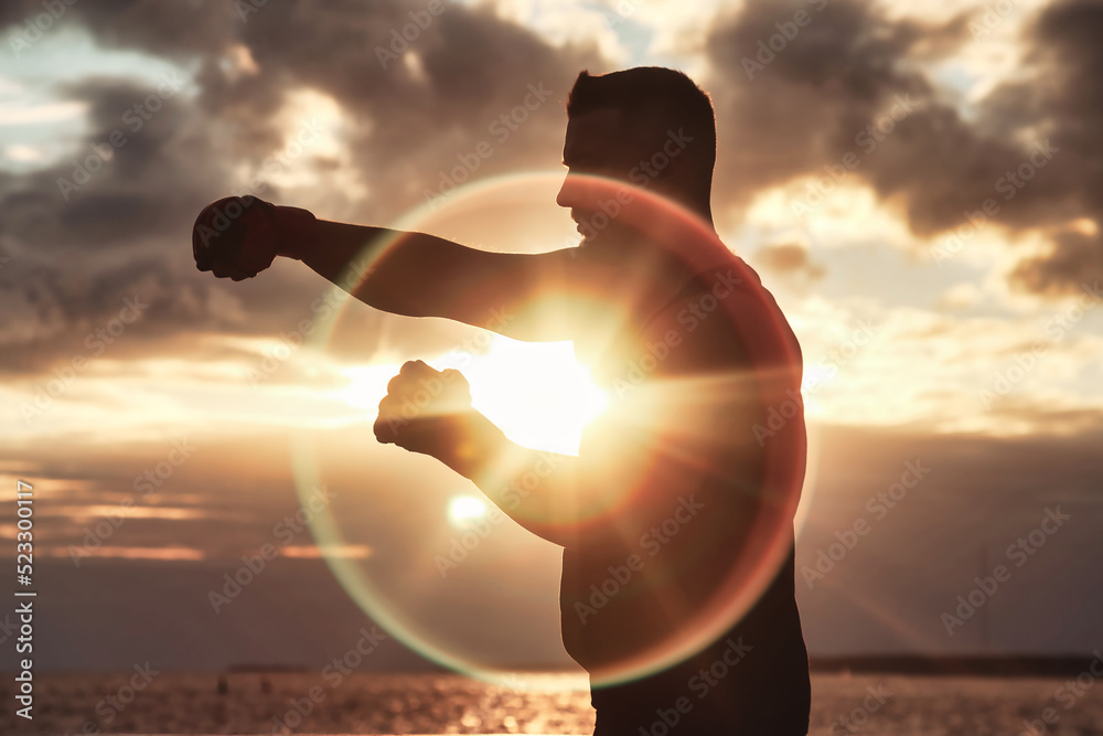 Silhouette of athlete man boxer fighter with boxing gloves posing fight and biceps at sunset background. Sports, healthy lifestyle and fitness training concept. Copy space