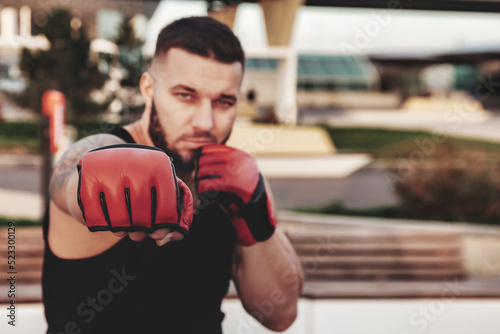 Athlete man boxer fighter with boxing gloves posing fight and biceps and looking at camera at urban background. Sport, healthy lifestyle and sports training concept. Copy space