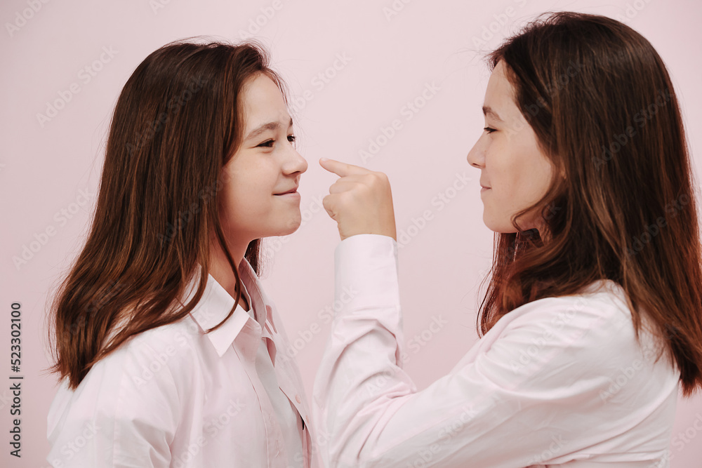 Fun playful twins standing face to face. One is reaching for nose of her sister Fun playful twins standing face to face. One is reaching for nose of her sister