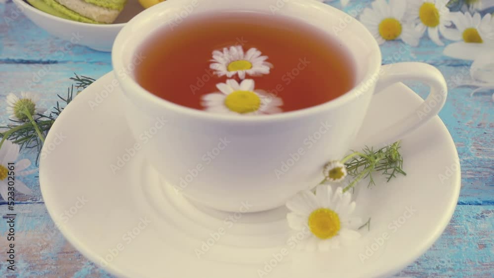 Composition with chamomile flowers and white cup of herbal tea on vintage light blue wooden table top. Summer theme. Composition with chamomile flowers and white cup of herbal tea on vintage light blue wooden table top. Summer theme.