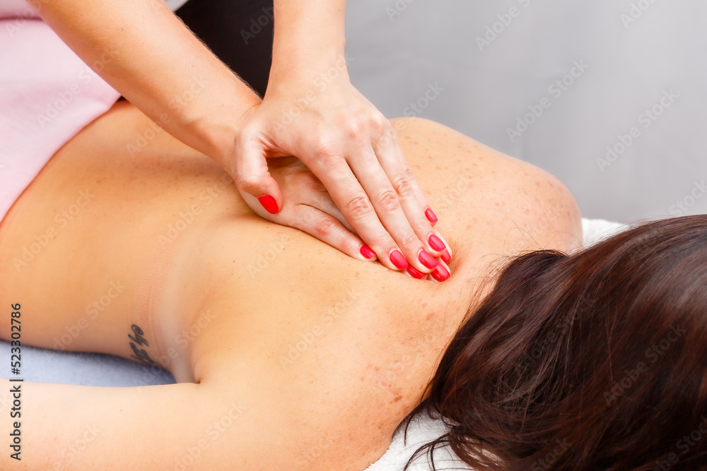 relaxed young woman lying face down on massage table enjoying therapeutic body massage by professional masseur in spa or wellness center