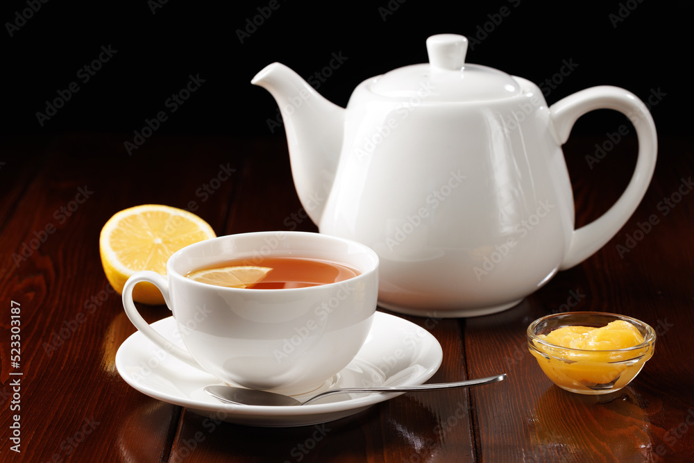 Tea with lemon and honey in a porcelain cup against a black background. Ceramic tea utensils. Side view. Selective focus. Tea with lemon and honey in a porcelain cup against a black background. Ceramic tea utensils. Side view. Selective focus.