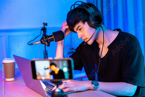 Playing video games on smartphone. Young asian handsome man sitting on chair holding cellphone in his hand. Exited streamer wearing headset  in neon room .Esport streaming game online.