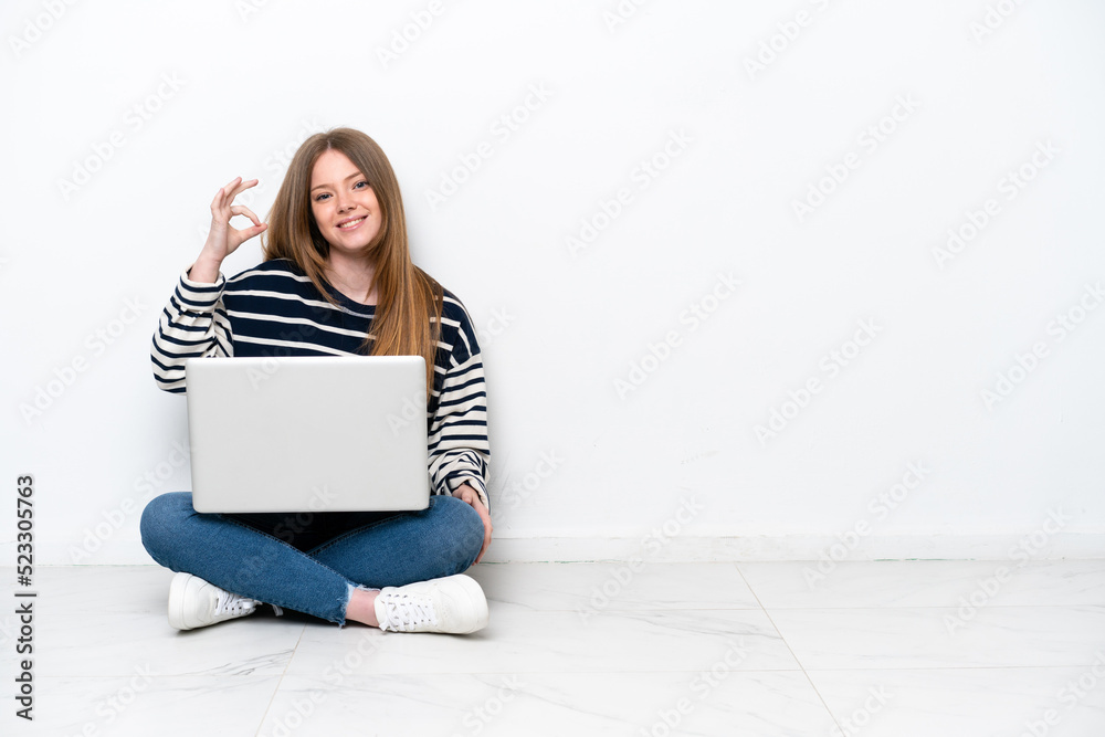 Young caucasian woman with a laptop sitting on the floor isolated on white background showing ok sign with fingers Young caucasian woman with a laptop sitting on the floor isolated on white background showing ok sign with fingers