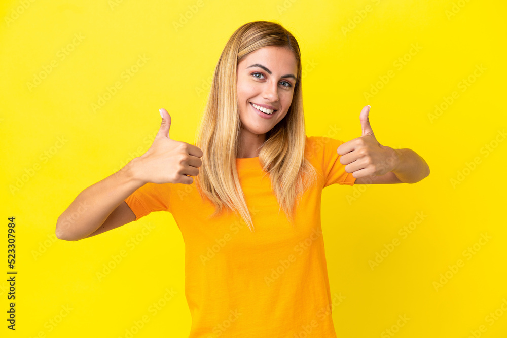 Blonde Uruguayan girl isolated on yellow background giving a thumbs up gesture Blonde Uruguayan girl isolated on yellow background giving a thumbs up gesture