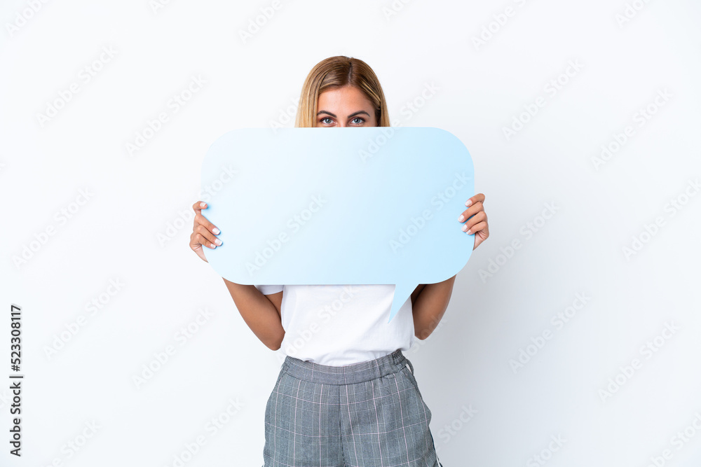 Blonde Uruguayan girl isolated on white background holding an empty speech bubble hiding behind it hiding behind it