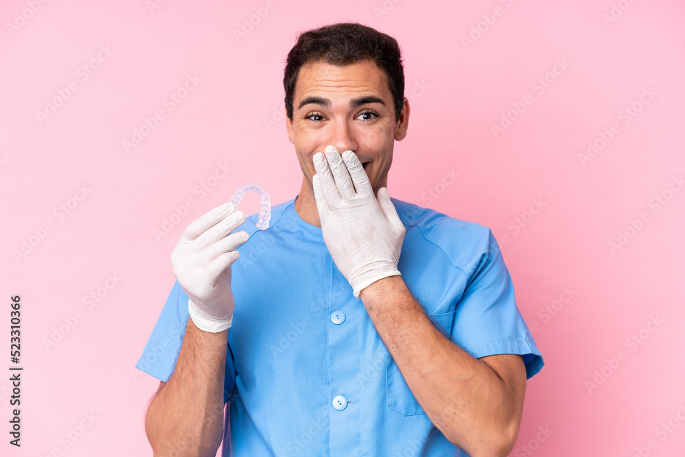 Dentist caucasian man holding invisible braces isolated on pink background happy and smiling covering mouth with hand Dentist caucasian man holding invisible braces isolated on pink background happy and smiling covering mouth with hand