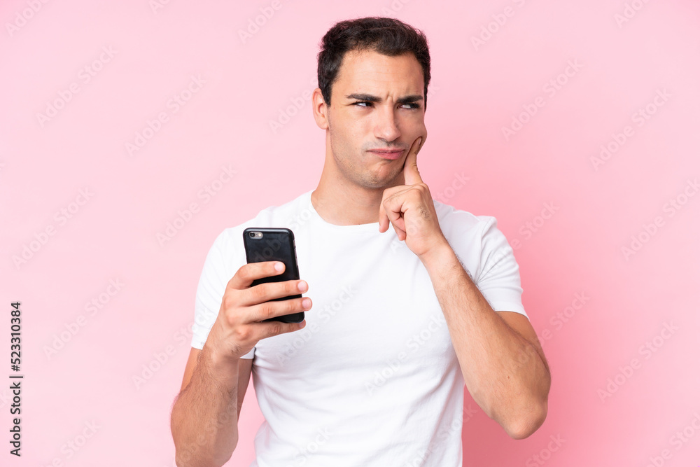Young caucasian man isolated on pink background using mobile phone and thinking Young caucasian man isolated on pink background using mobile phone and thinking