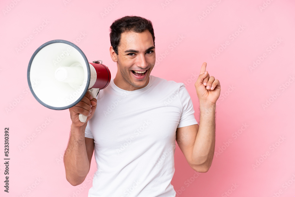 Young caucasian man isolated on pink background shouting through a megaphone and pointing side Young caucasian man isolated on pink background shouting through a megaphone and pointing side