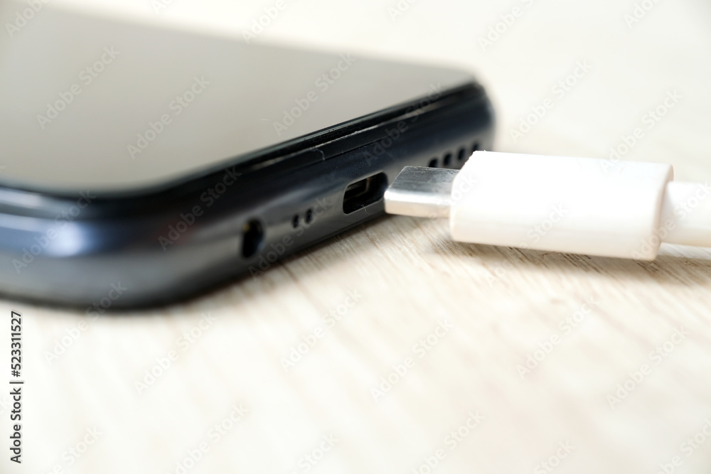 Modern smartphone charging on wooden table. Modern technology concept. Selective focus Modern smartphone charging on wooden table. Modern technology concept. Selective focus