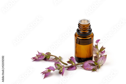 A bottle of essential oil with fresh blooming clary sage twigs on white background.