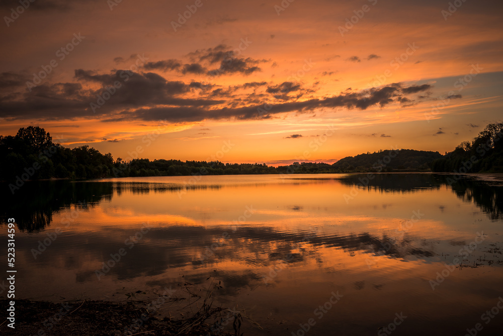 Epic red and gold clouds over forest lake at sunset. Dramatic cloud cover. Symmetrical reflections on the water, natural mirror. idyllic landscape.