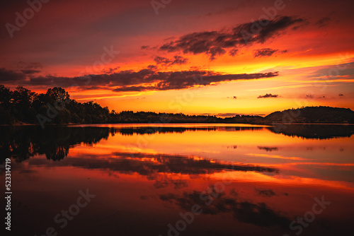 Epic red and gold clouds over forest lake at sunset. Dramatic cloud cover. Symmetrical reflections on the water, natural mirror. idyllic landscape.