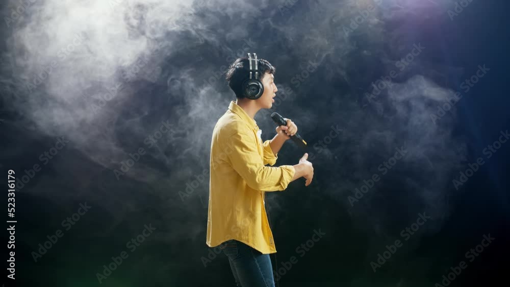 Side View Of Young Asian Boy With Headphone Holding A Microphone And Rapping On The White Smoke Black Background
Side View Of Young Asian Boy With Headphone Holding A Microphone And Rapping On The White Smoke Black Background