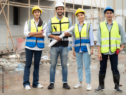 Construction engineer hold house blueprint working with architect, building contractor and foreman at estate site. Project manager meeting discussion with teamwork. Diverse group of people teamwork.