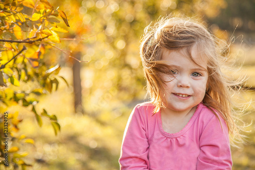 Young girl on a windy day smiling next to a deciduous tree