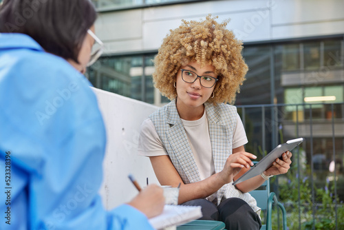 Talented employees collaborate together make researchers in websites on digital tablet connected to wireless internet discuss creative ideas take notes pose in cafeteria against blurred background