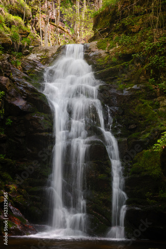 Scenic  sunlit waterfall in the forest cascading down the moss covered cliff