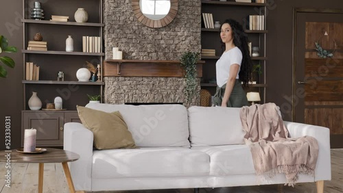 Funny young comedy woman blogger comical hides behind sofa recording humorous vlog plays hide-and-seek cheerful playful girl fooling around kidding in living room looking at camera smiling having fun