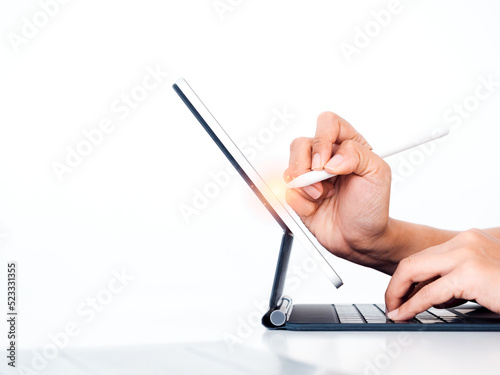 Electric pencil in business person s hand  writing or drawing on digital tablet screen while typing on keyboard computer isolated on white background with copy space  side view. Work with technology.