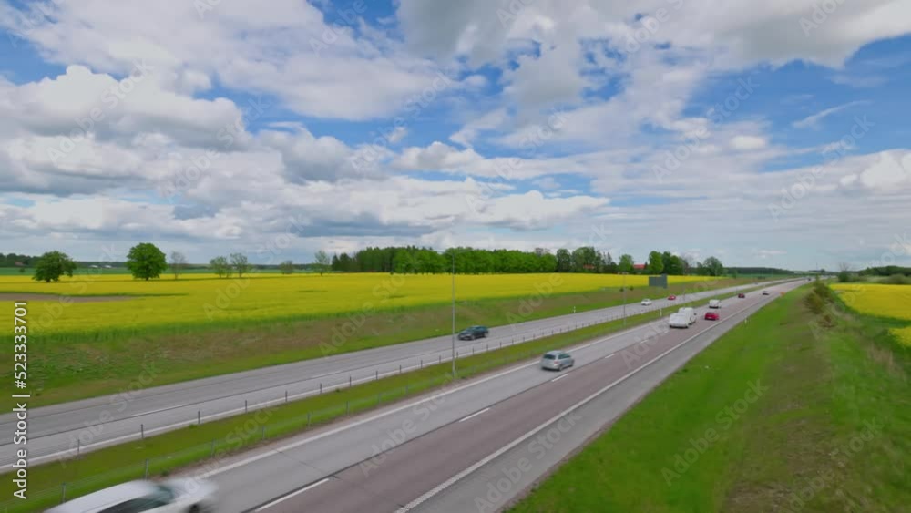Beautiful top view of highway with moving cars. Rapeseed fields with white clouds against sky. Sweden. Beautiful top view of highway with moving cars. Rapeseed fields with white clouds against sky. Sweden.