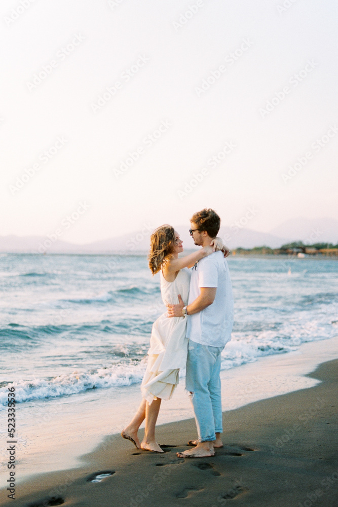 Man hugs woman while standing on the beach. Side view