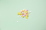 White yellow and pink medical pills of different sizes close-up on a green background.