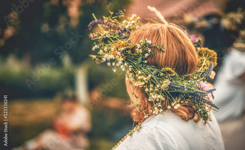 Woman in flower wreath on sunny meadow, Floral crown, symbol of summer solstice.
