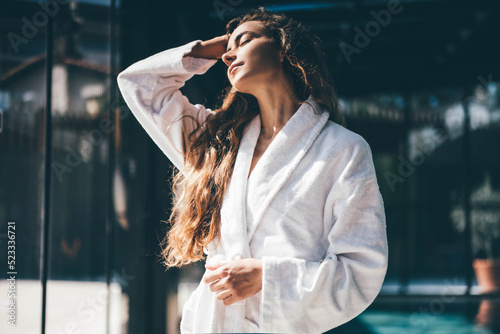 Young woman in white bathrobe walking near swimming pool on background. photo