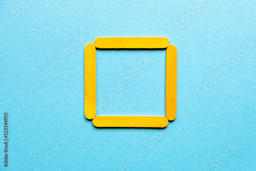 yellow square made of wooden sticks on a blue background. Geometric figure. Hobbies for children. Wooden sticks for construction