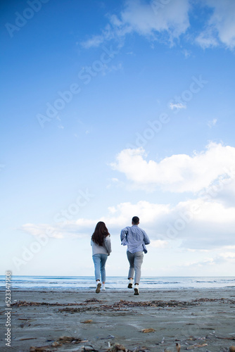 Young couple from behind is running at the beach to the sea in Larnaca, Cyprus