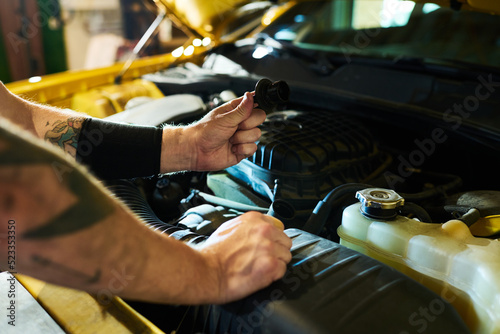 Hands of young man holding detail of car engine over open hood while checking up motor and choosing suitable spare parts before repair