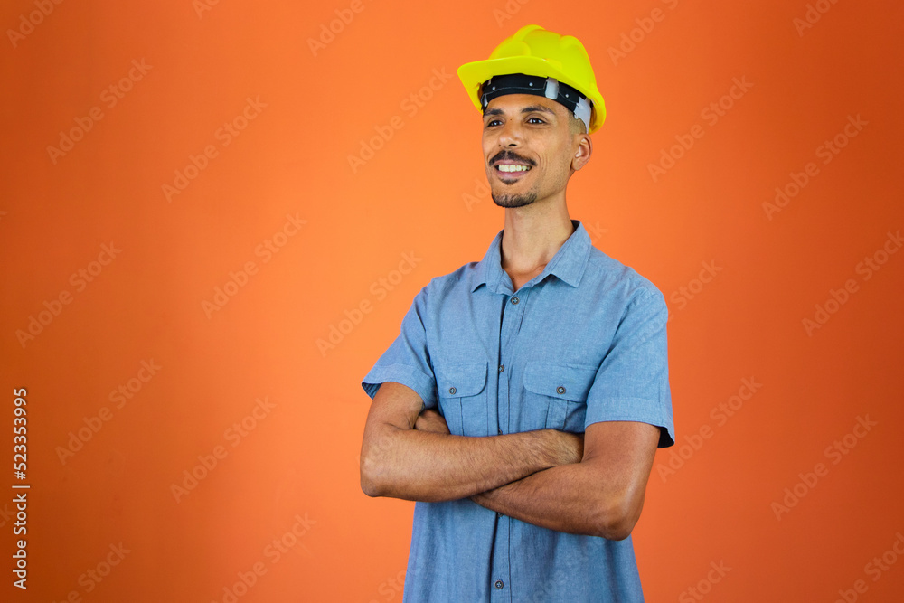 Engineers day - Black Man in Safety Helmet and Blue Shirt isolated on orange. Engineers day - Black Man in Safety Helmet and Blue Shirt isolated on orange.