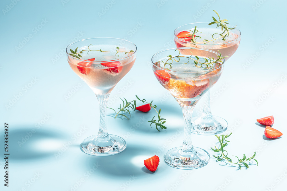 Glass of strawberry cocktail or mocktail, refreshing summer drink with champagne, strawberries, ice cubes and rosemary on blue background Glass of strawberry cocktail or mocktail, refreshing summer drink with champagne, strawberries, ice cubes and rosemary on blue background