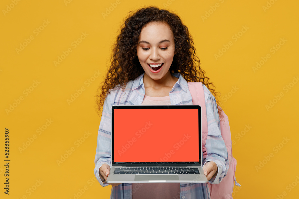 Naklejka premium Young black teen girl student she wear casual clothes backpack bag hold laptop pc computer blank screen workspace area isolated on plain yellow color background High school university college concept.