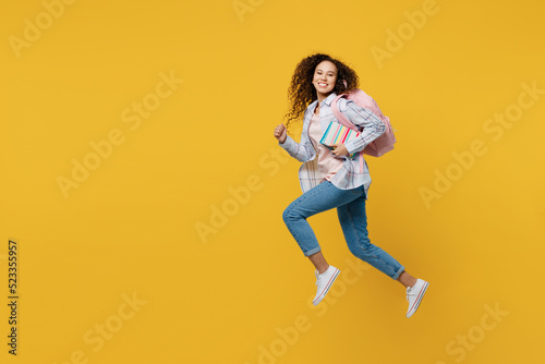 Full body young black teen girl student she wear casual clothes backpack bag jump high look camera run fast hurrying isolated on plain yellow color background. High school university college concept.