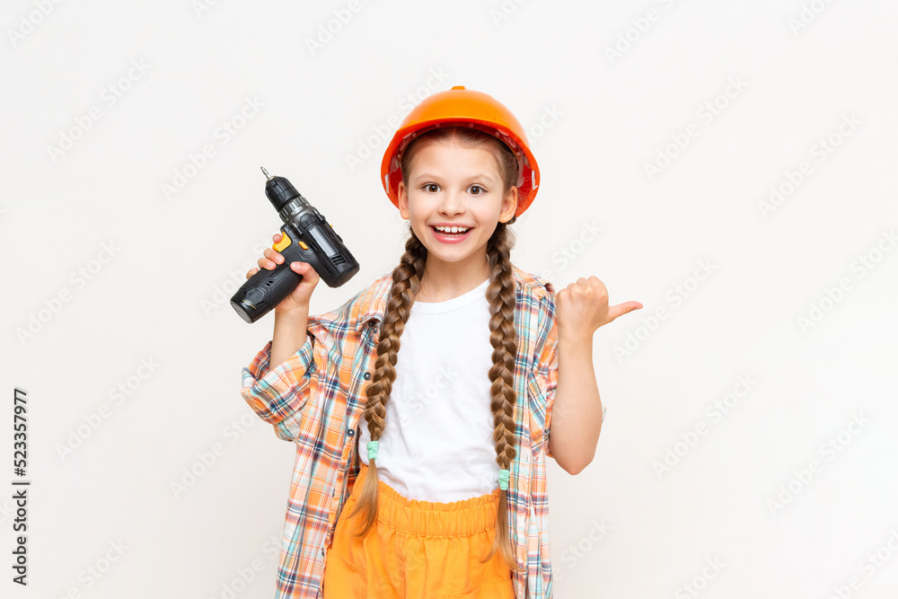 A little girl with a drill in her hands to show your advertisement on a white isolated background. The concept of renovation in the children's room. A little girl with a drill in her hands to show your advertisement on a white isolated background. The concept of renovation in the children's room.