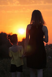 Mom and daughter at sunset. A woman and a child are walking against the backdrop of the sunset.