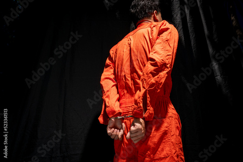 Handcuffs on Accused Criminal in Orange Jail Jumpsuit. Law Offender Sentenced to Serve Jail Time, in black background.