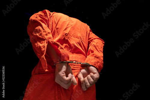 Handcuffs on Accused Criminal in Orange Jail Jumpsuit. Law Offender Sentenced to Serve Jail Time, in black background.