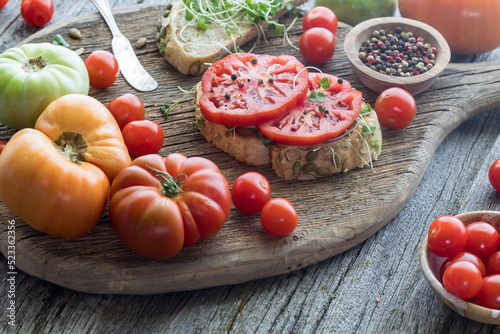 Open faced heirloom tomato sandwich on a rustic board with tomatoes all around.